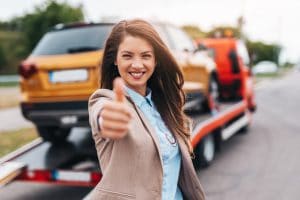 Lächelnde Frau zeigt Daumen hoch vor Abschleppwagen – Symbolbild für Kundenzufriedenheit mit Motorschaden-Ankauf.de.